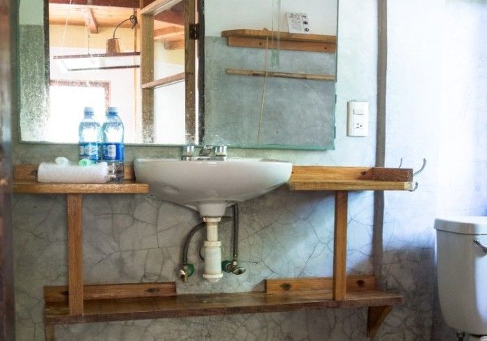 Baño con lavabo blanco, espejo, estantes de madera y pared alicatada en posada del arquitecto en mazunte, oaxaca