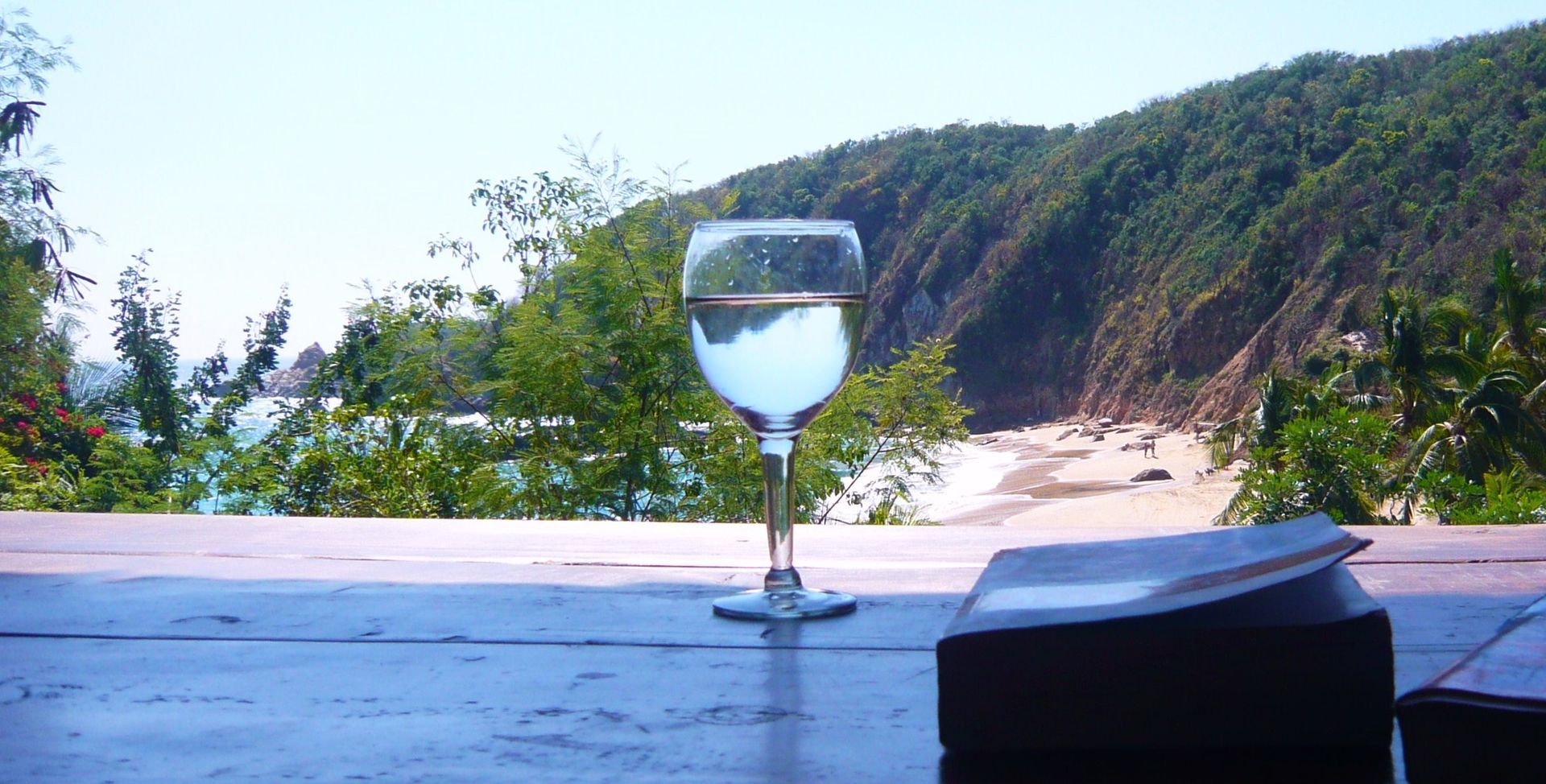 Vaso de agua sobre una mesa de madera, playa y colinas al fondo en mazunte, oaxaca