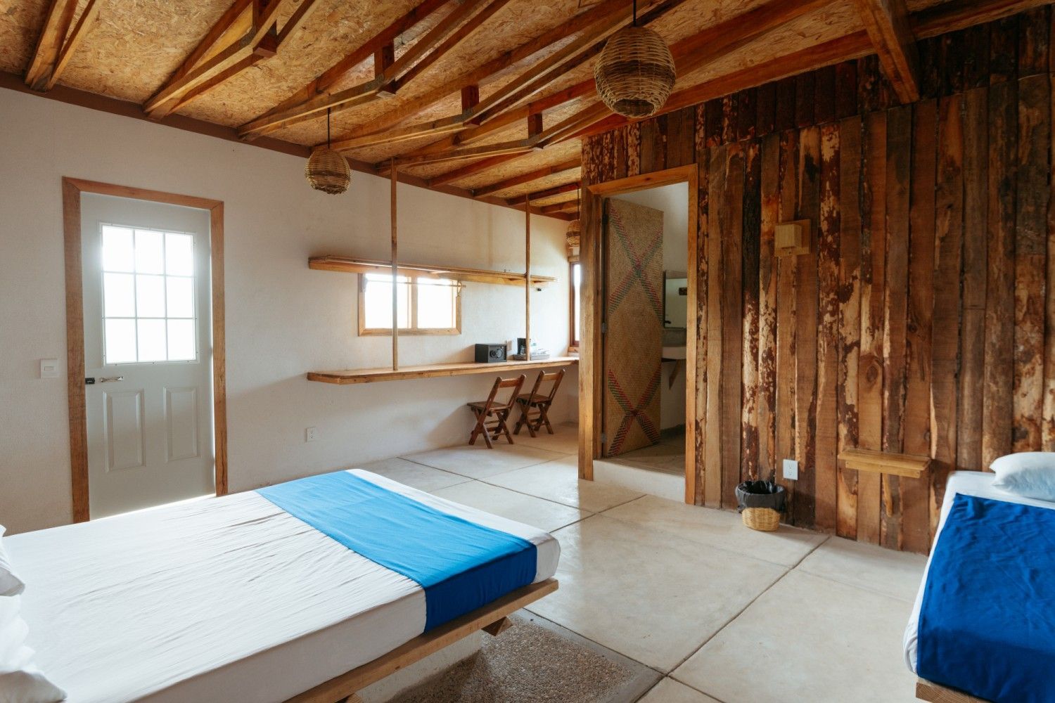 Dormitorio con paredes y techo de madera rústica, dos camas y una zona de escritorio en mazunte, oaxaca