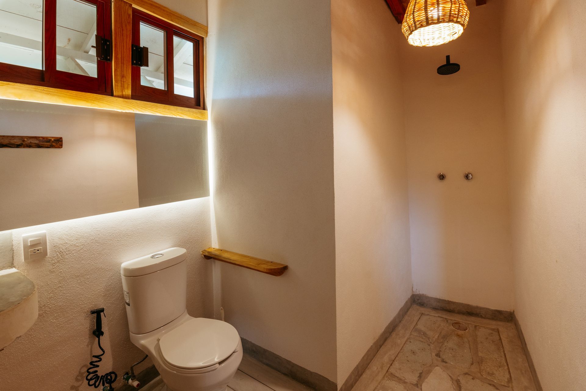 Baño pequeño con paredes blancas, inodoro, zona de ducha y detalles de madera en posada del arquitecto en mazunte, oaxaca