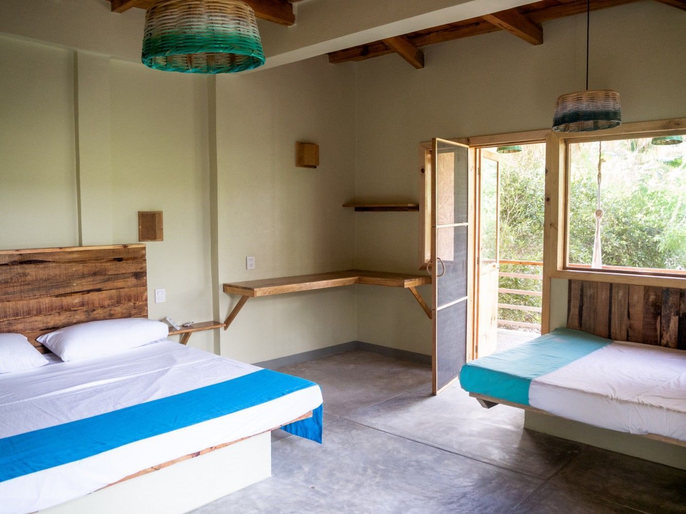 Dormitorio con camas de madera, escritorio y puerta a un balcón en posada del arquitecto en mazunte, oaxaca