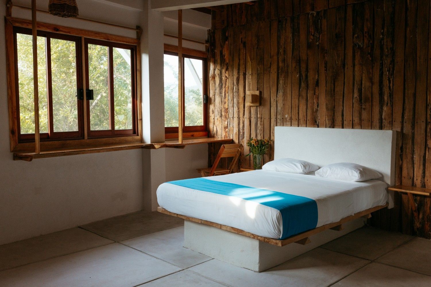 Dormitorio con pared decorativa de madera y dos ventanas con vistas al exterior en posada del arquitecto en mazunte, oaxaca