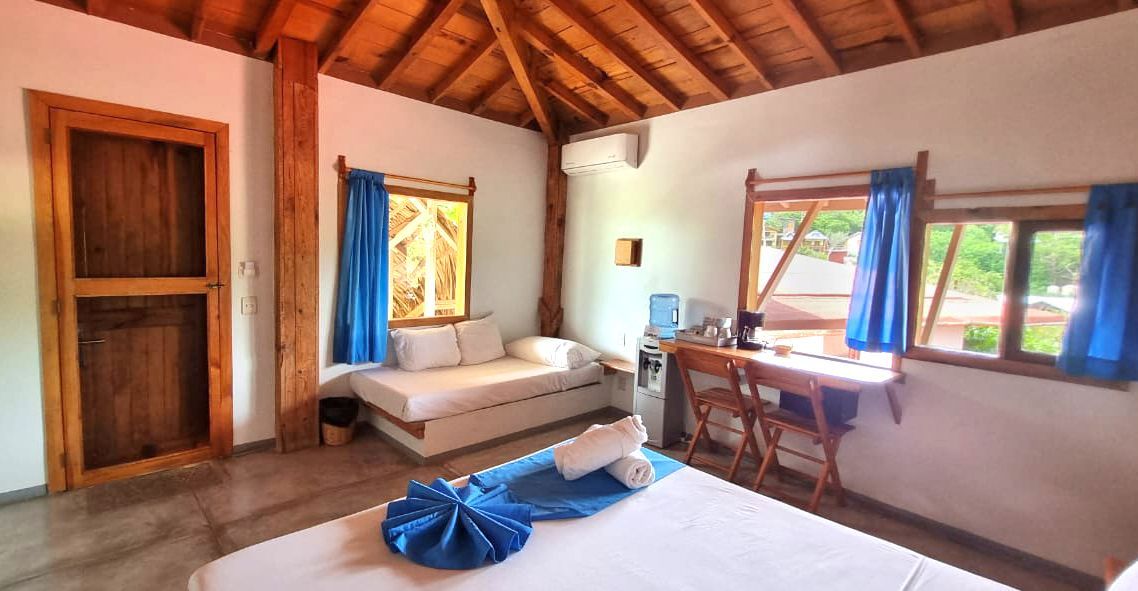 Dormitorio con paredes blancas, techo y puerta de madera en posada del arquitecto en mazunte, oaxaca