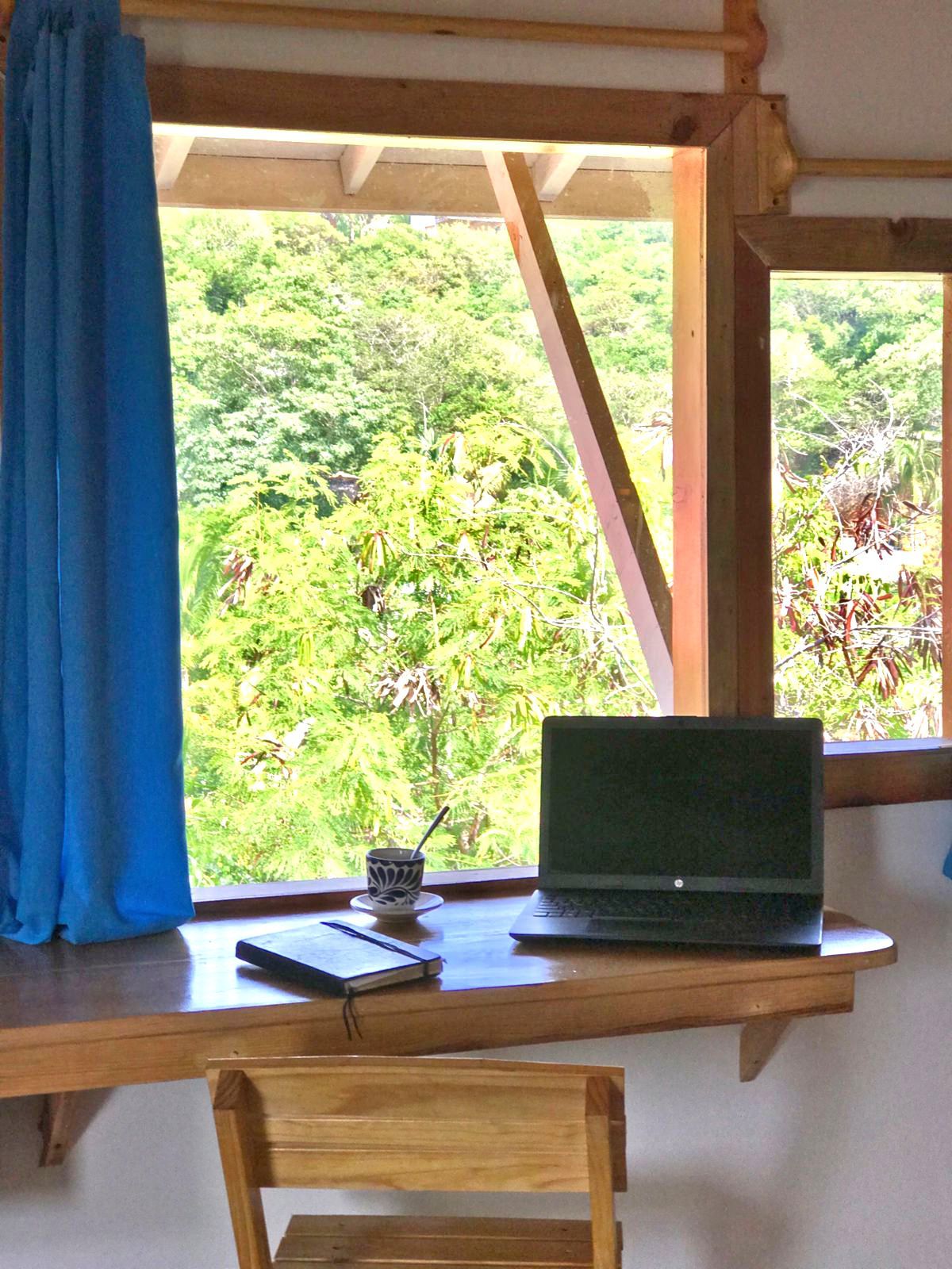 escritorio de madera junto a una ventana con vistas a frondosos árboles verdes en mazunte, oaxaca