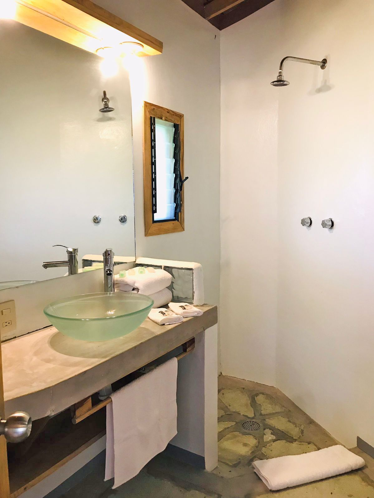 Baño con lavabo, ducha, suelo de piedra y molduras de madera en posada del arquitecto en mazunte, oaxaca