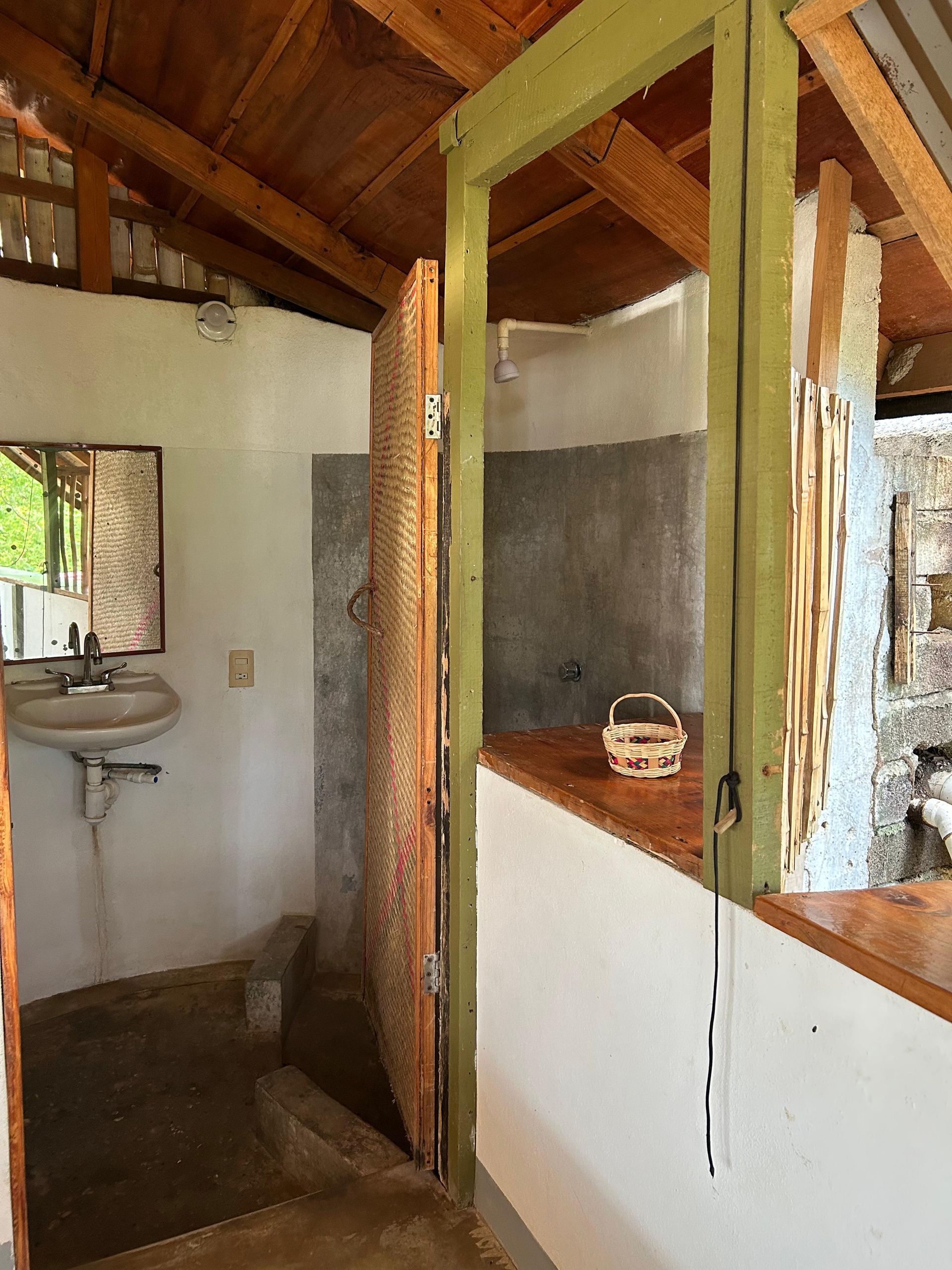 Baño con puerta de madera, lavabo, ducha y vigas a la vista en posada del arquitecto en mazunte, oaxaca