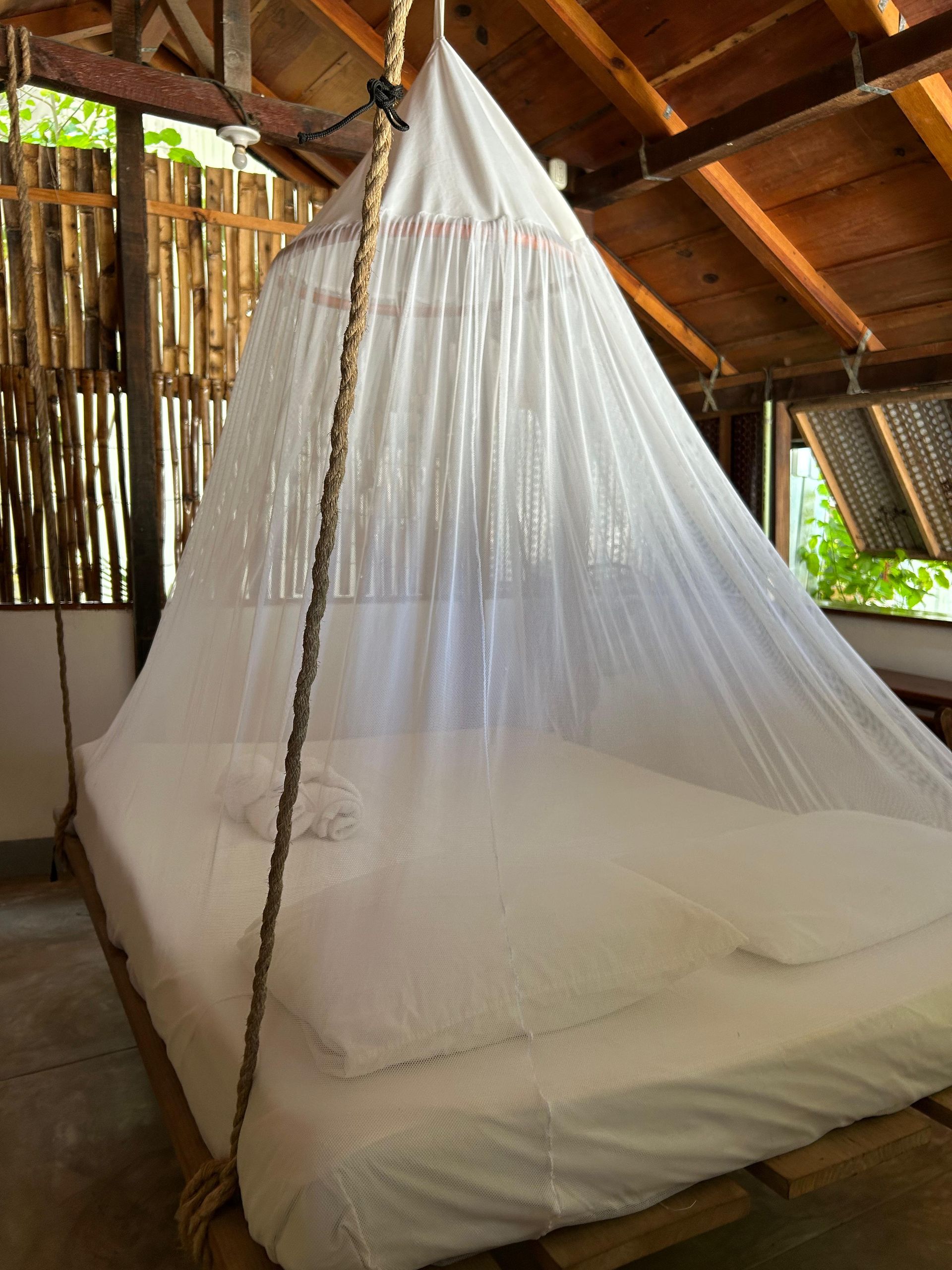 Cama con sábanas blancas y mosquitera colgando del techo de madera en en posada del arquitecto en mazunte, oaxaca