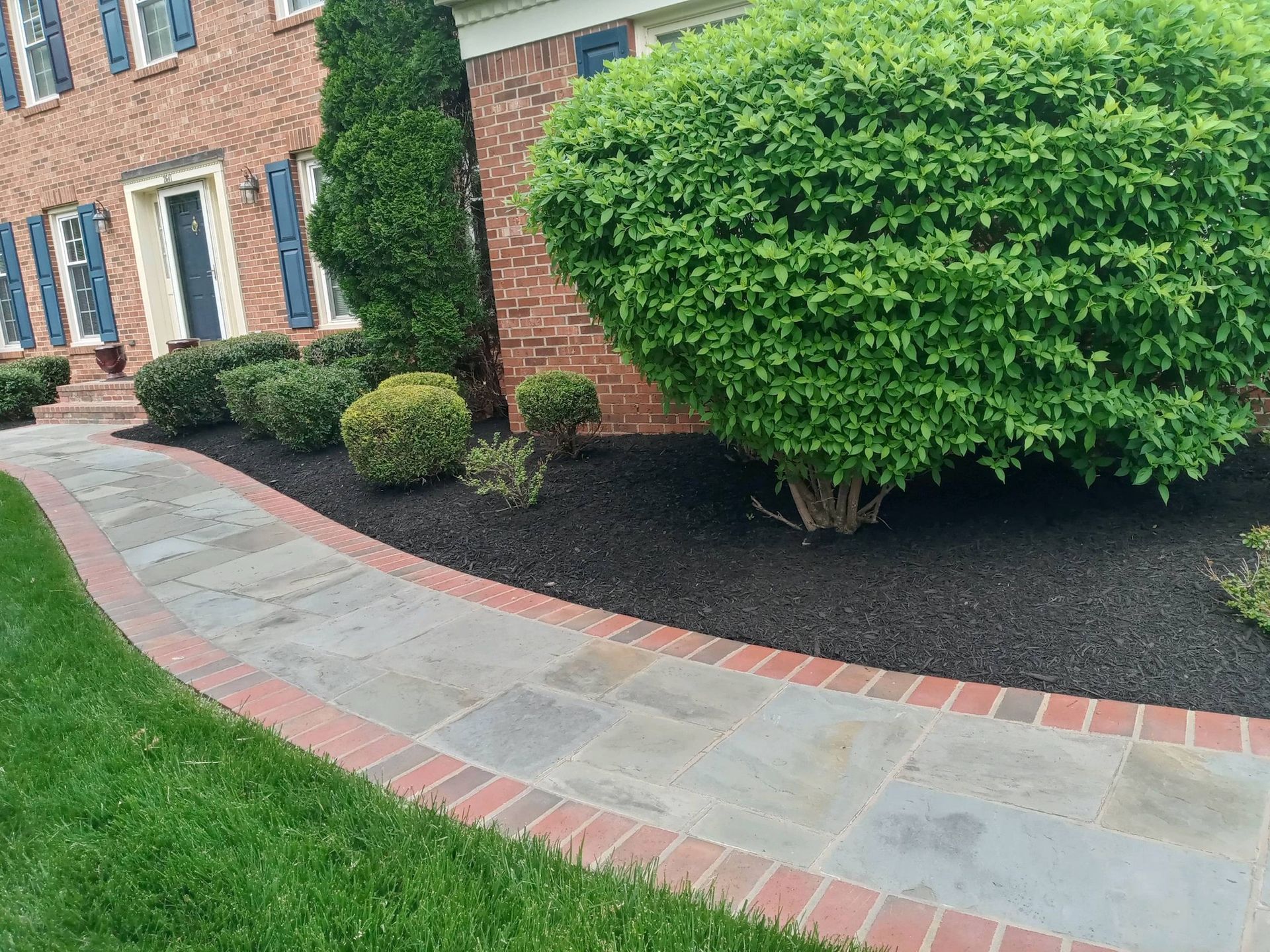 A walkway leading to a brick house with a lush green lawn.