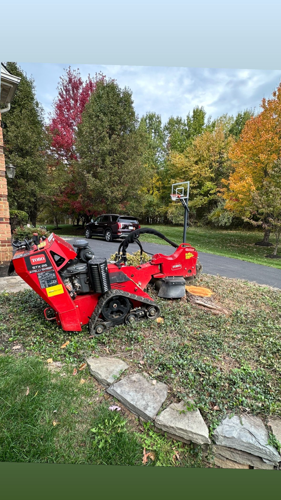 A red lawn mower is sitting in the grass in front of a house.