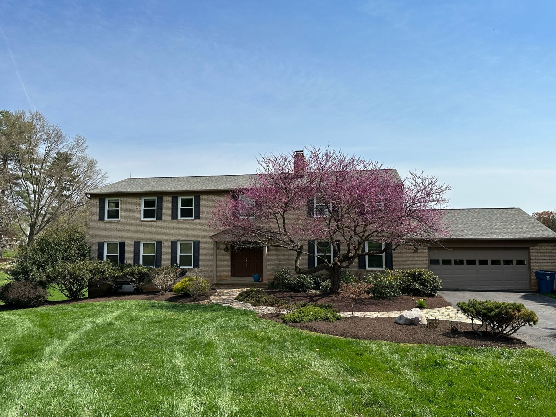 A large house with a lush green lawn and a cherry blossom tree in front of it.
