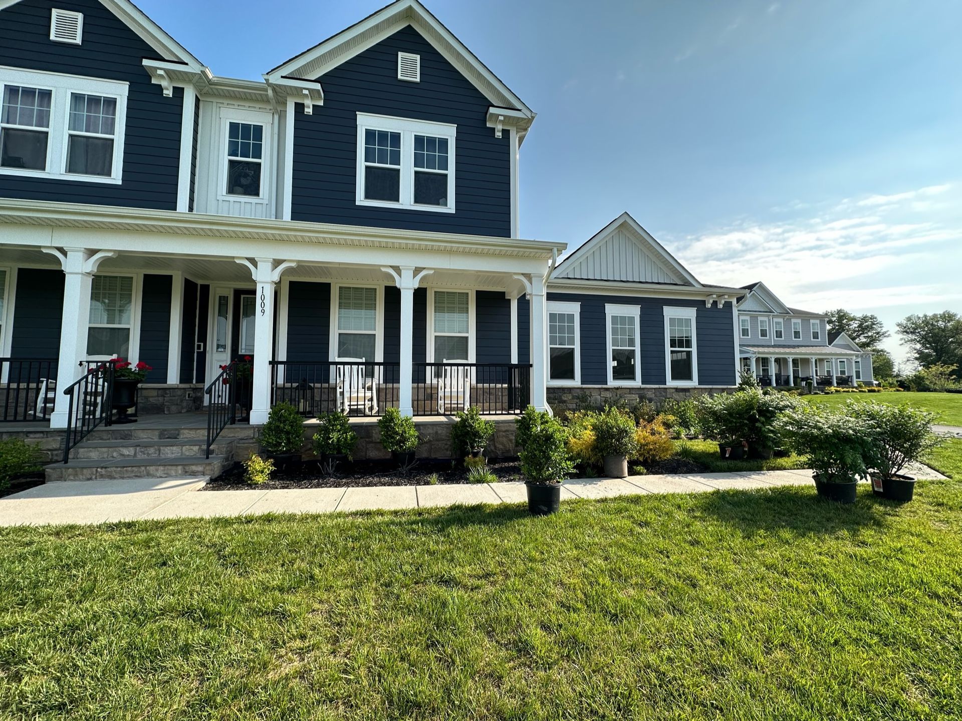A large black and white house with a large porch is sitting on top of a lush green field.