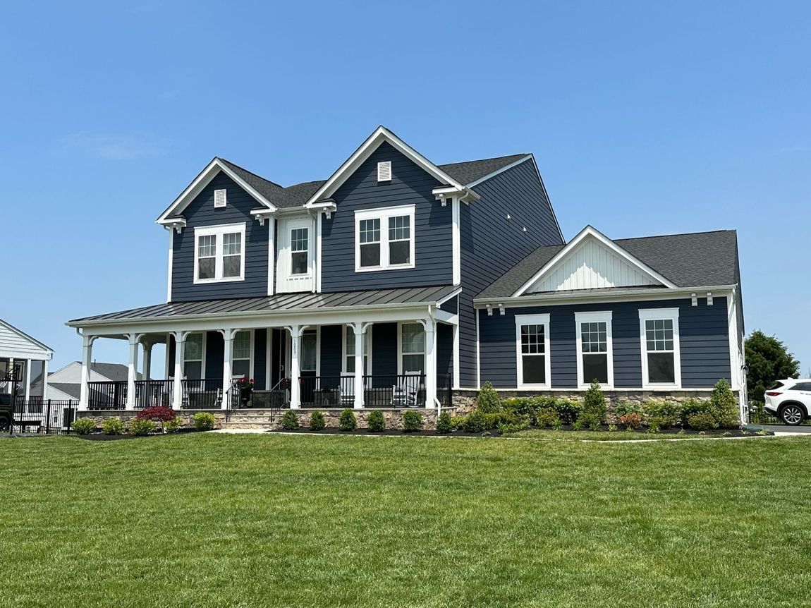 A large house with a large porch is sitting on top of a lush green field.