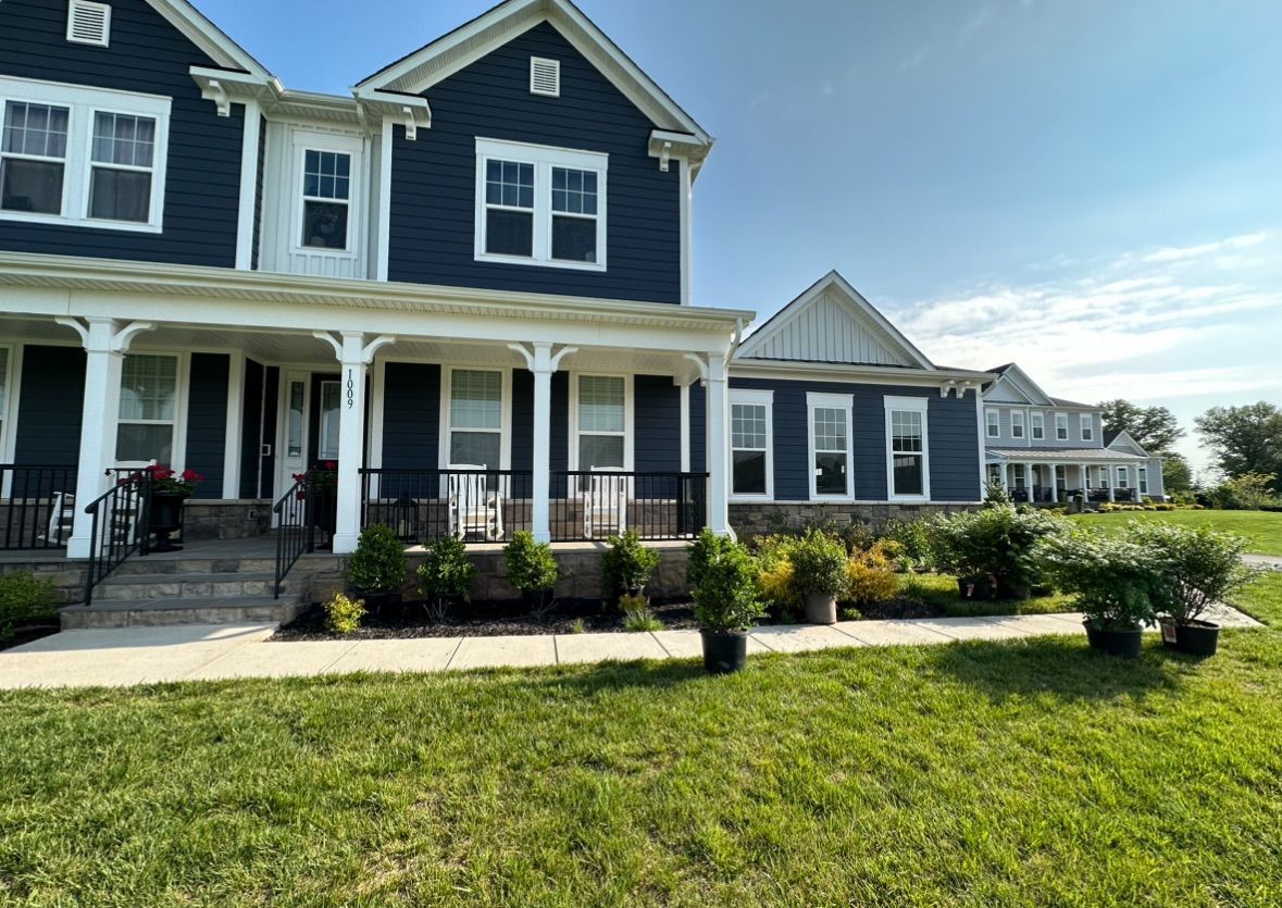 A large blue house with a white porch and a large lawn in front of it.