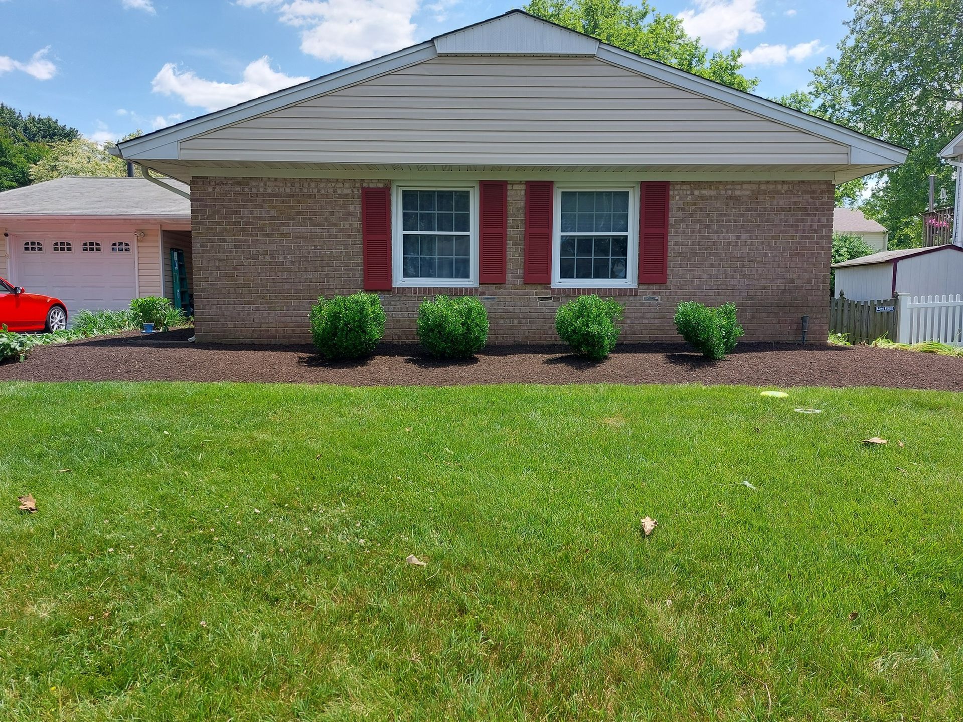 A brick house with red shutters and a red car parked in front of it.