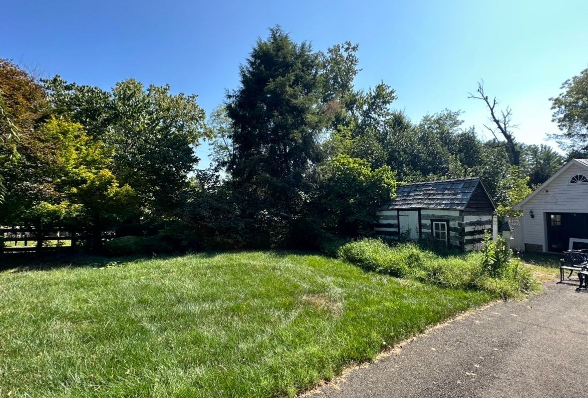 A shed is sitting in the middle of a grassy field next to a garage.