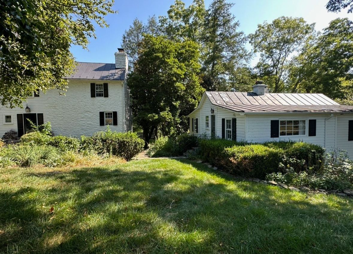 A large white house with black shutters is surrounded by trees and grass.