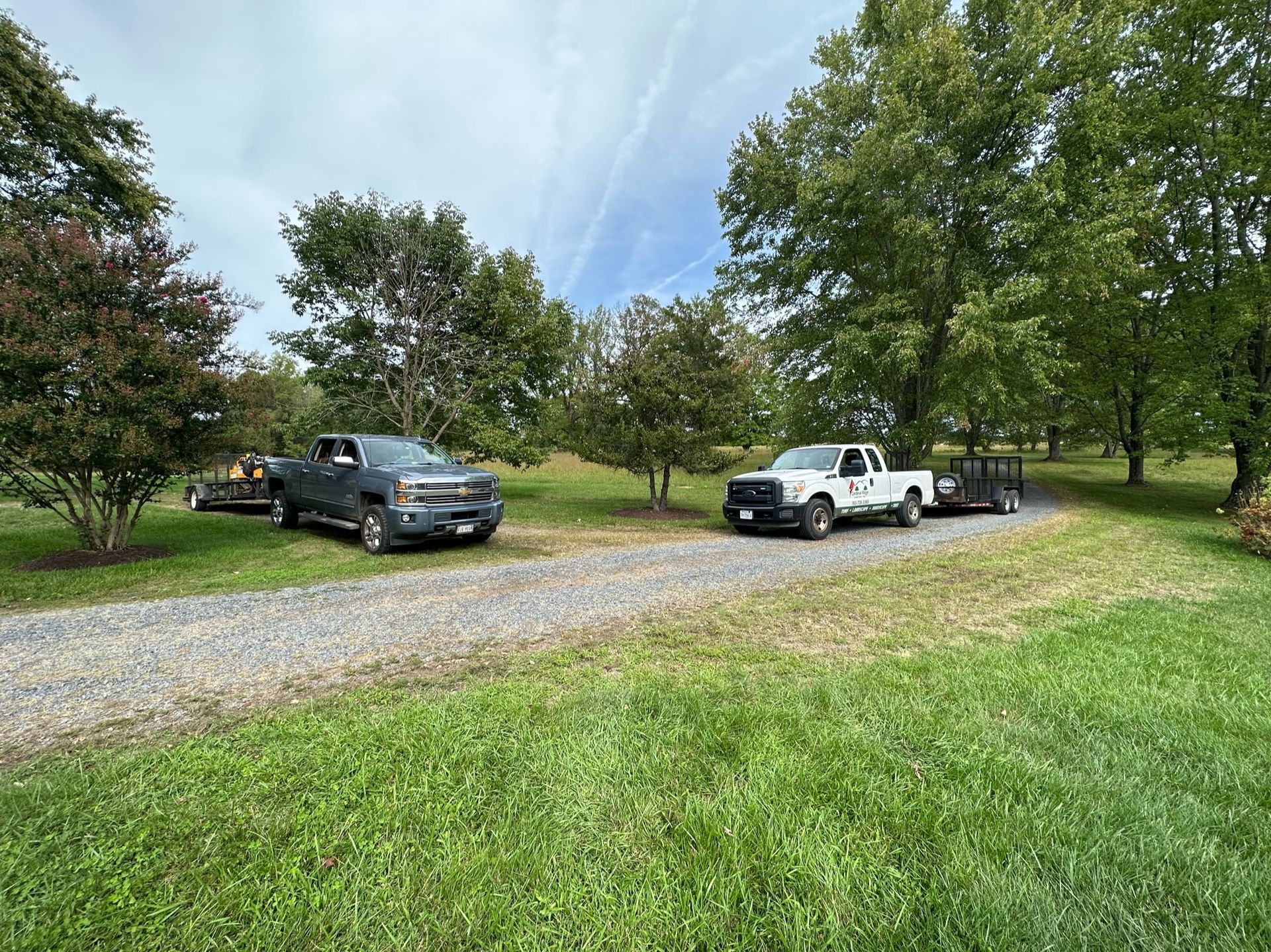 Two trucks are parked on a gravel road in a grassy field.