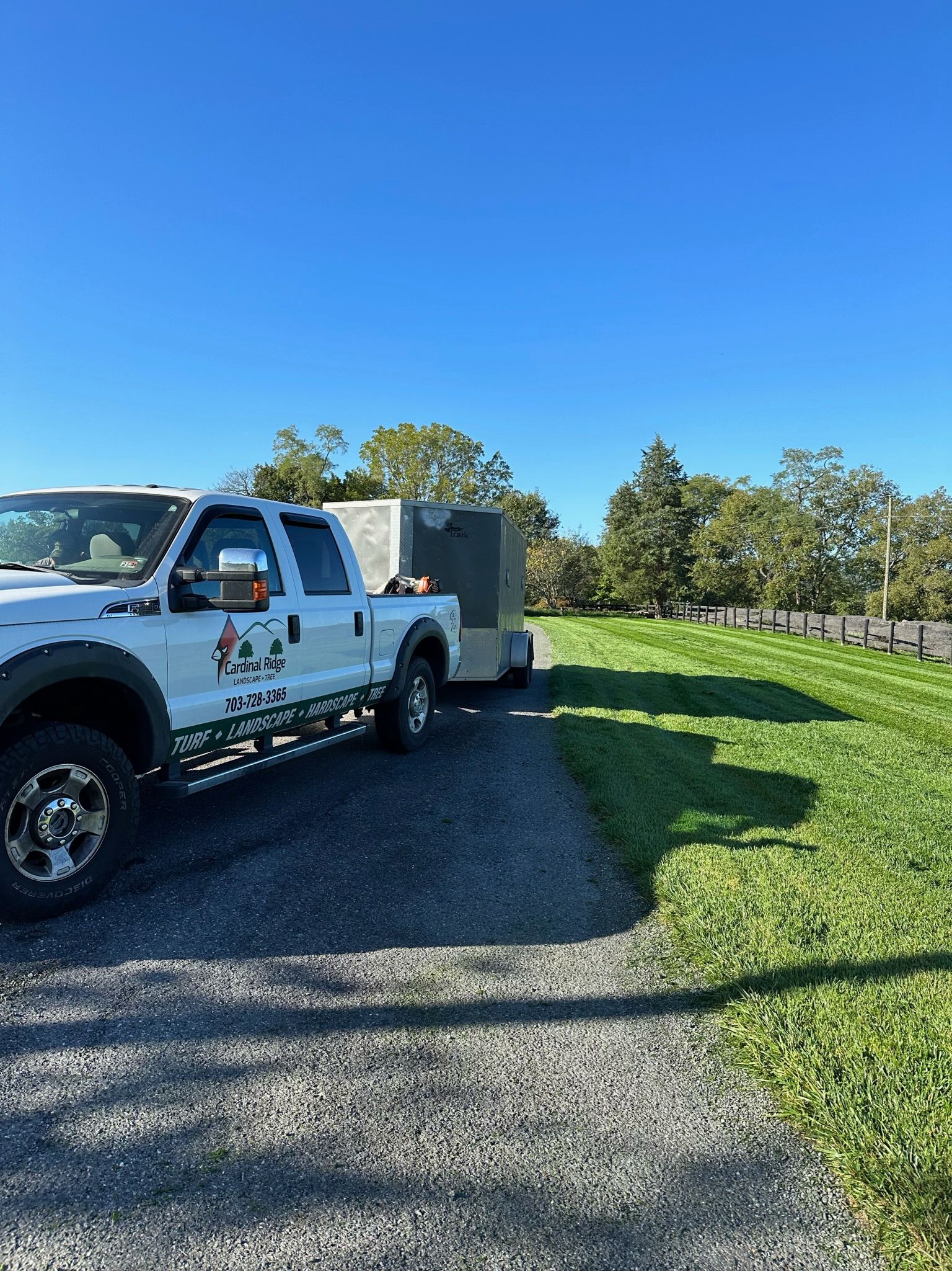 A white truck is parked on a gravel road next to a trailer.