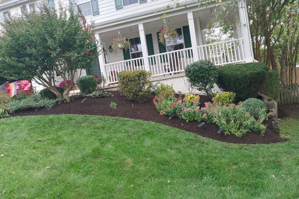 A white house with a porch and a lush green lawn in front of it.