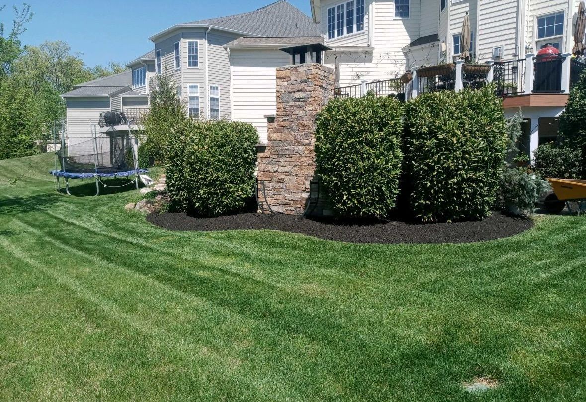 A lush green lawn with a stone fireplace in the middle of it in front of a house.