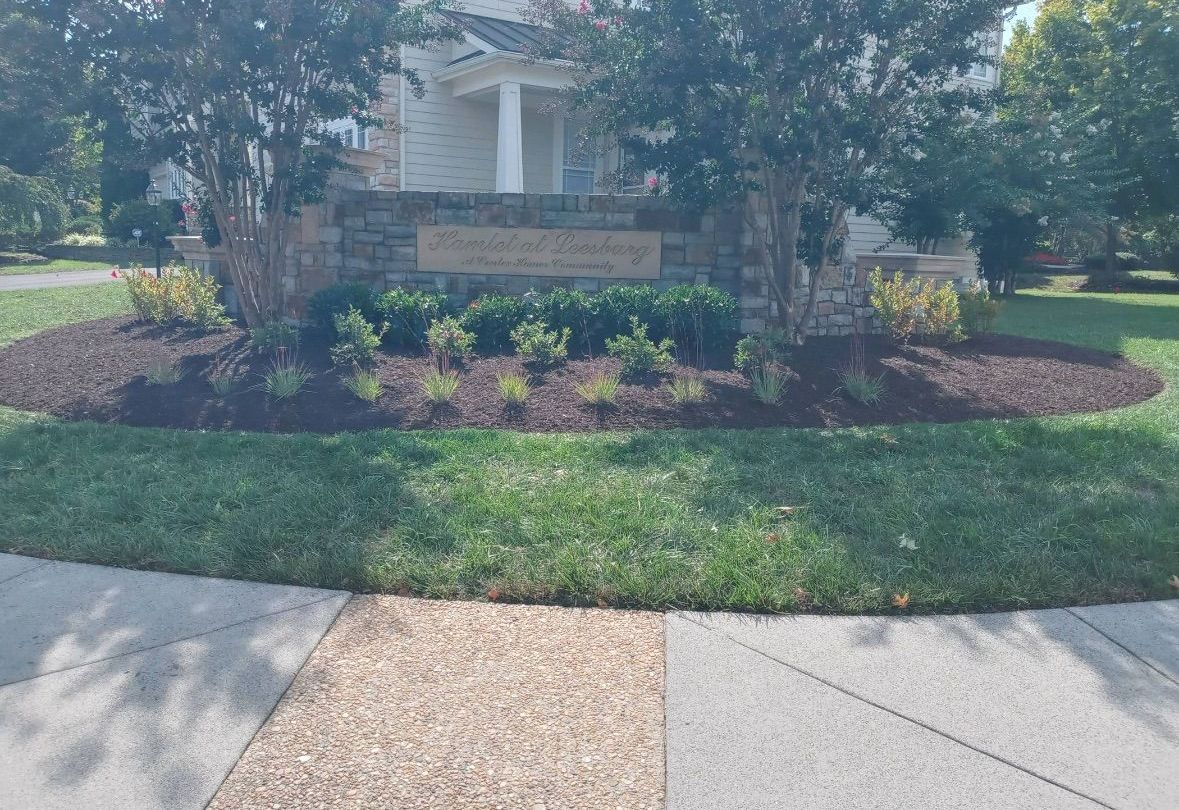 A lawn with a stone wall and a sign in front of a house.