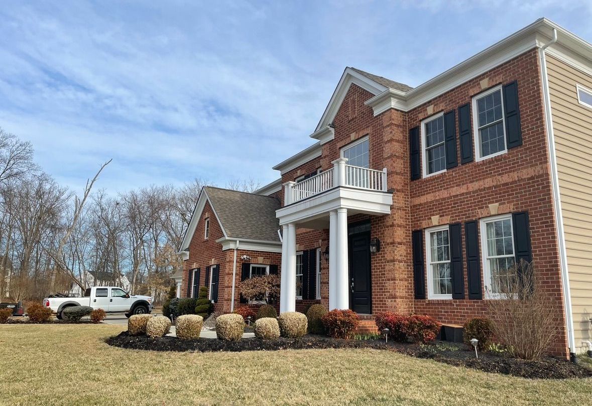 A large brick house with black shutters and a white truck parked in front of it.