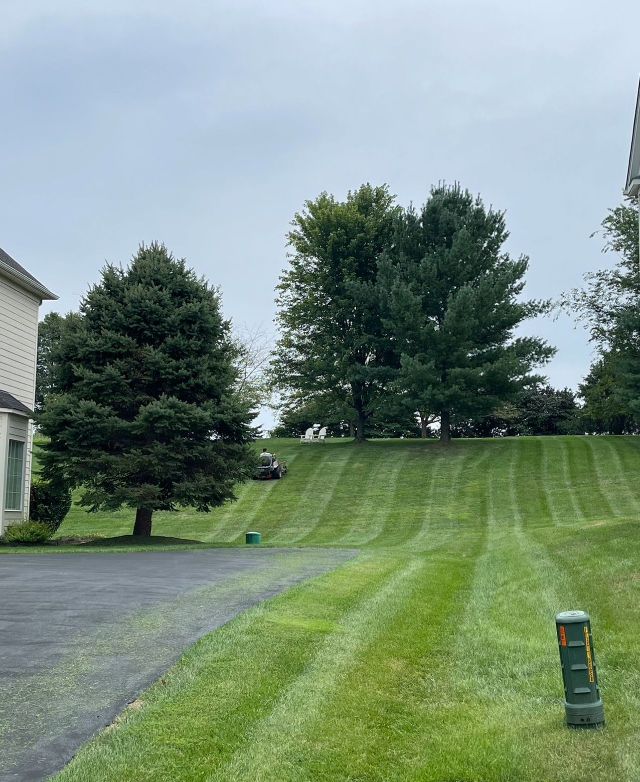 A lawn mower is cutting a lush green lawn in front of a house.