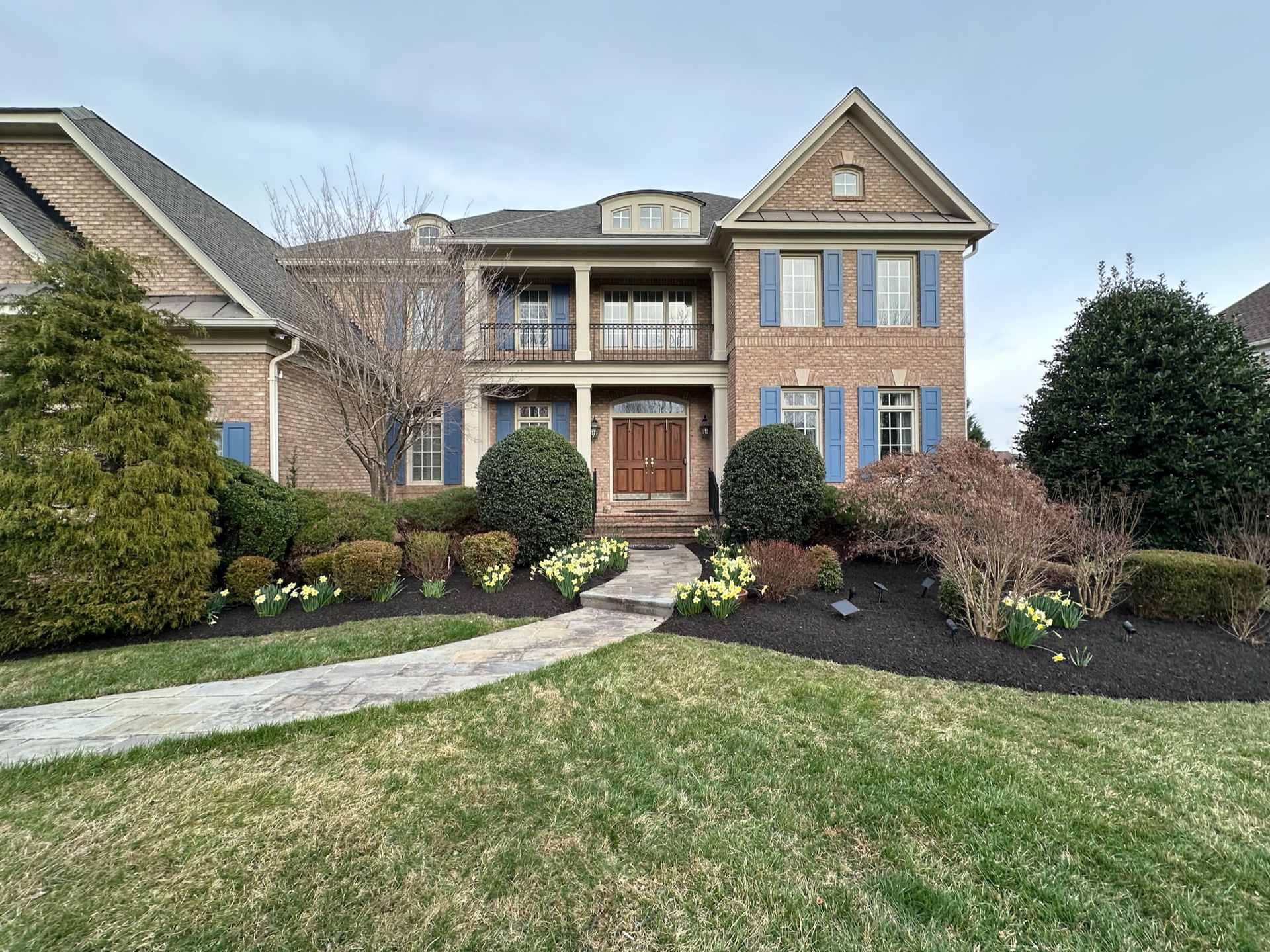 A large brick house with blue shutters and a walkway leading to it.
