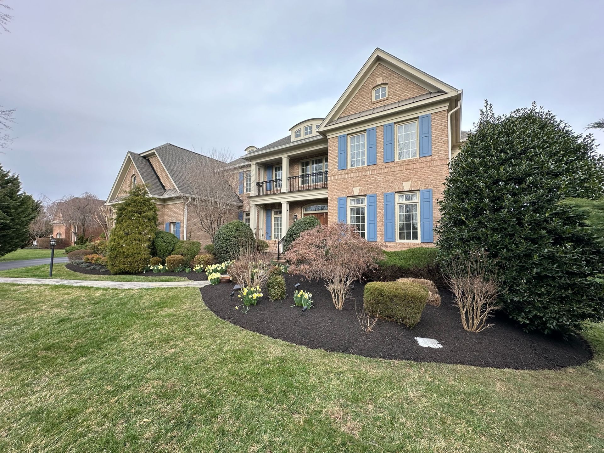 A large brick house with blue shutters is sitting on top of a lush green lawn.