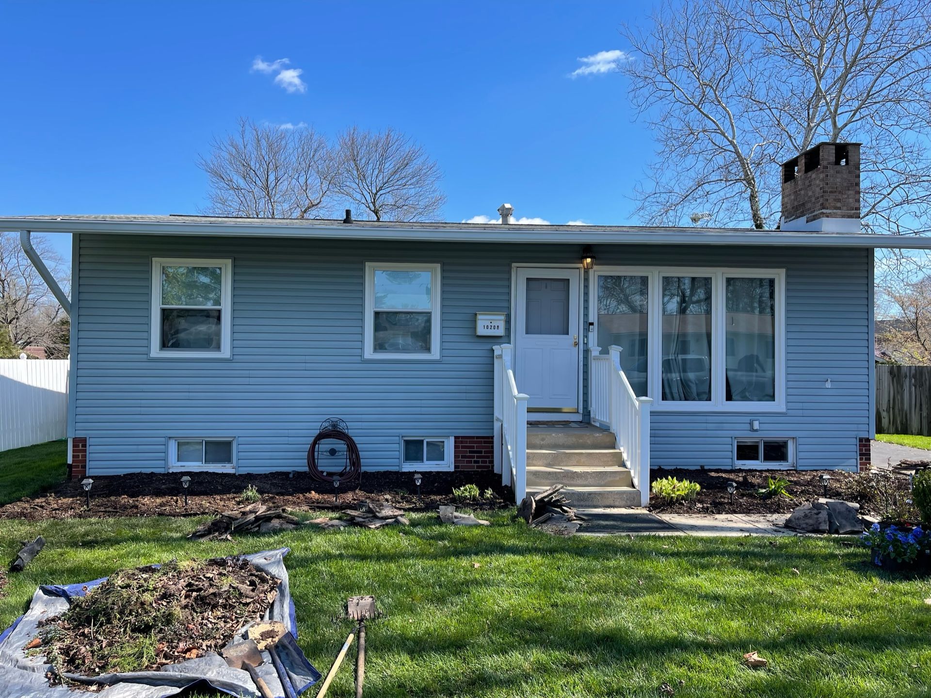 A blue house with a white door and stairs is sitting on top of a lush green lawn.
