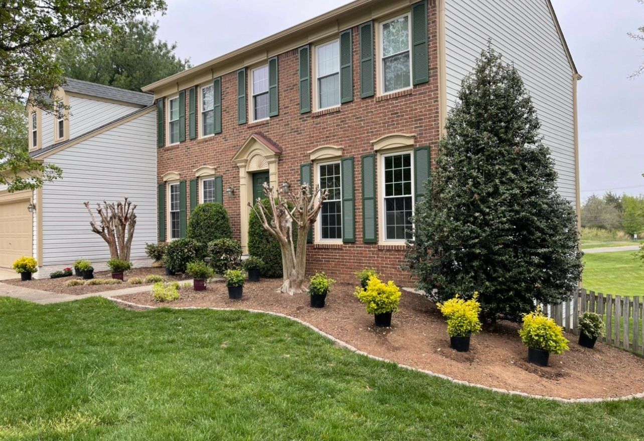 A brick house with green shutters and potted plants in front of it.