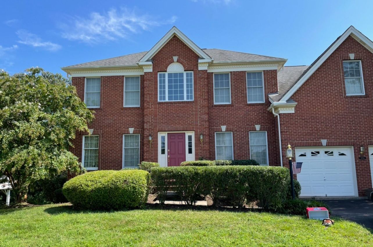 A large brick house with a white garage door is sitting on top of a lush green lawn.