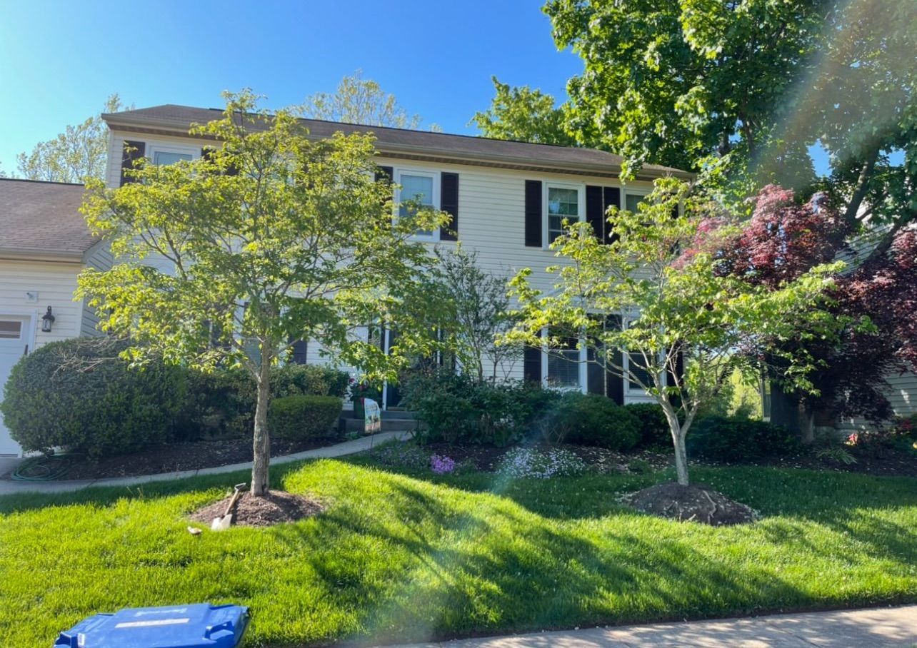 A white house with a brown roof and a blue trash can in front of it.