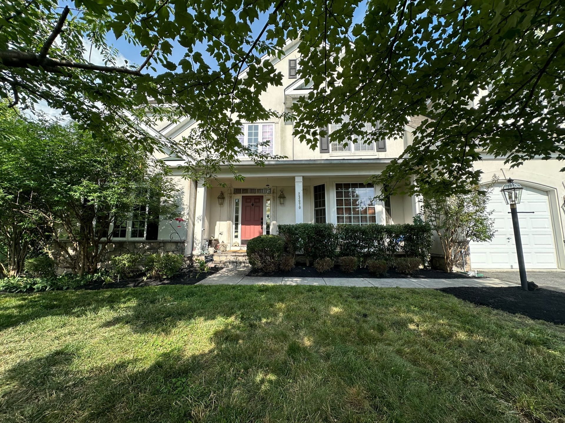 A large white house with a red door is surrounded by trees and grass.