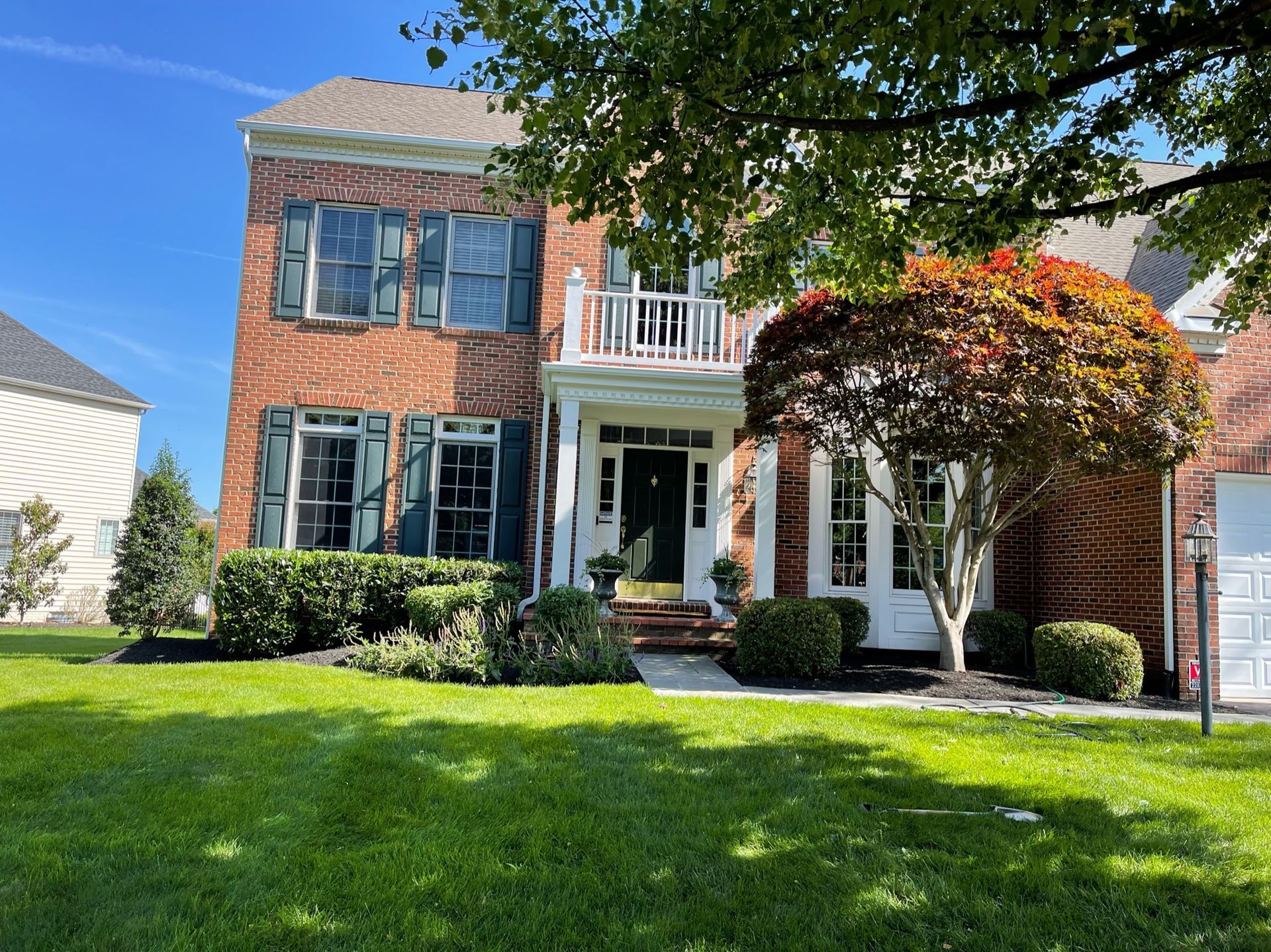 A large brick house with blue shutters and a large lawn in front of it.