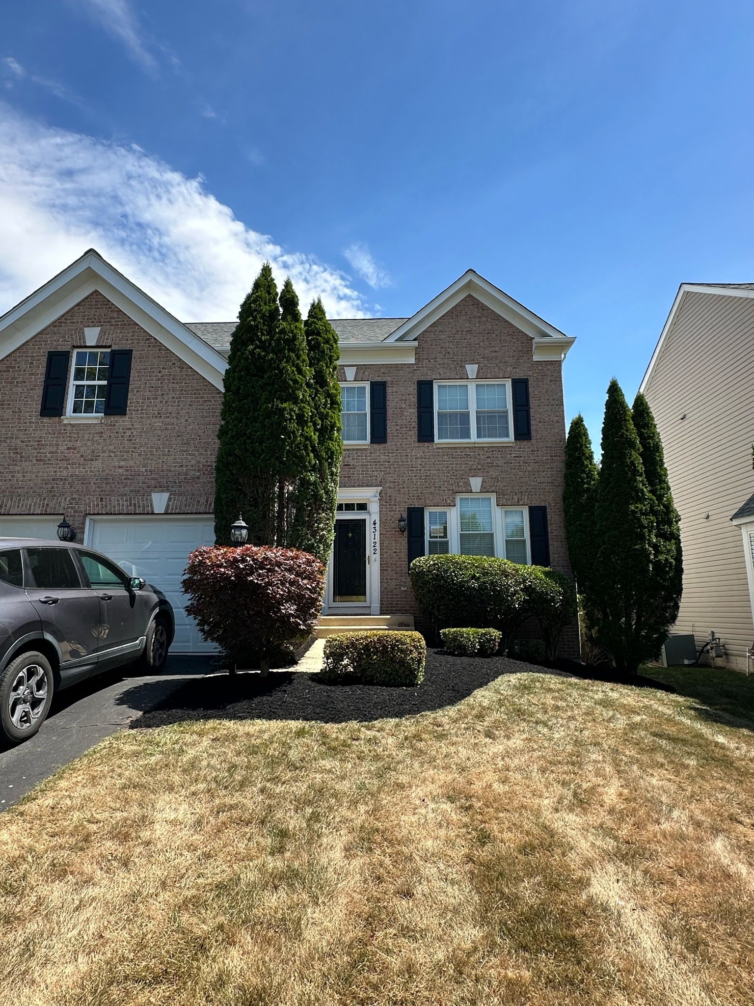 A car is parked in front of a large brick house.