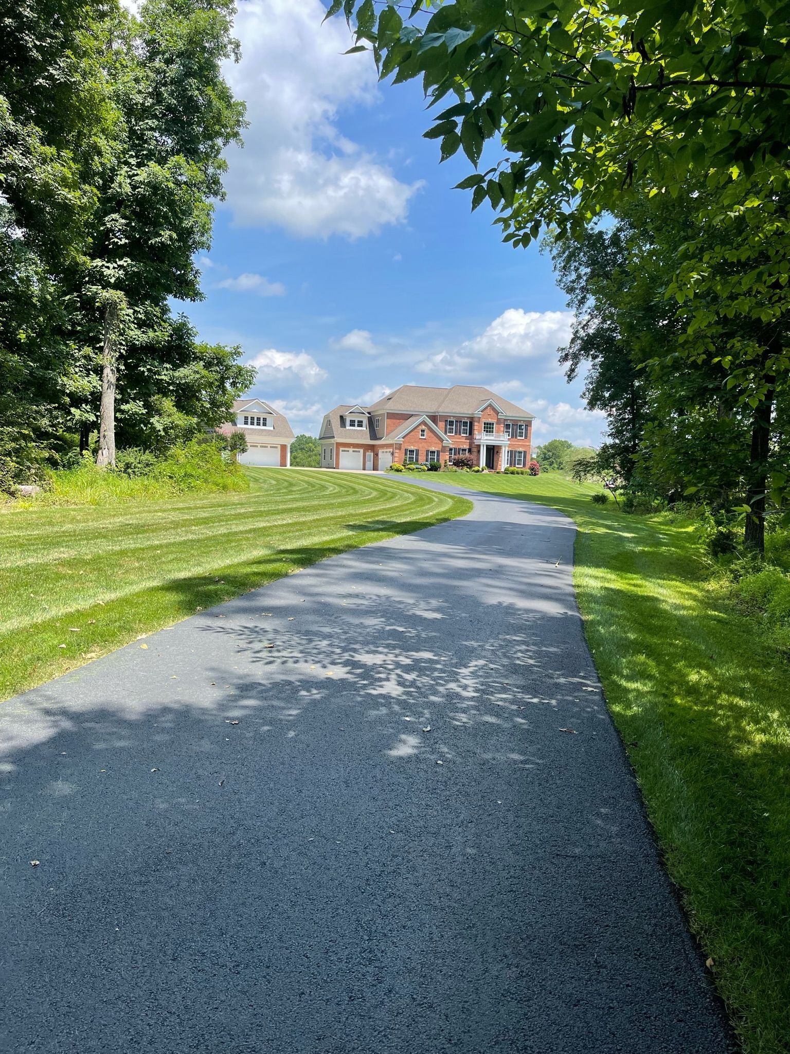A road going through a grassy field with a house in the background.