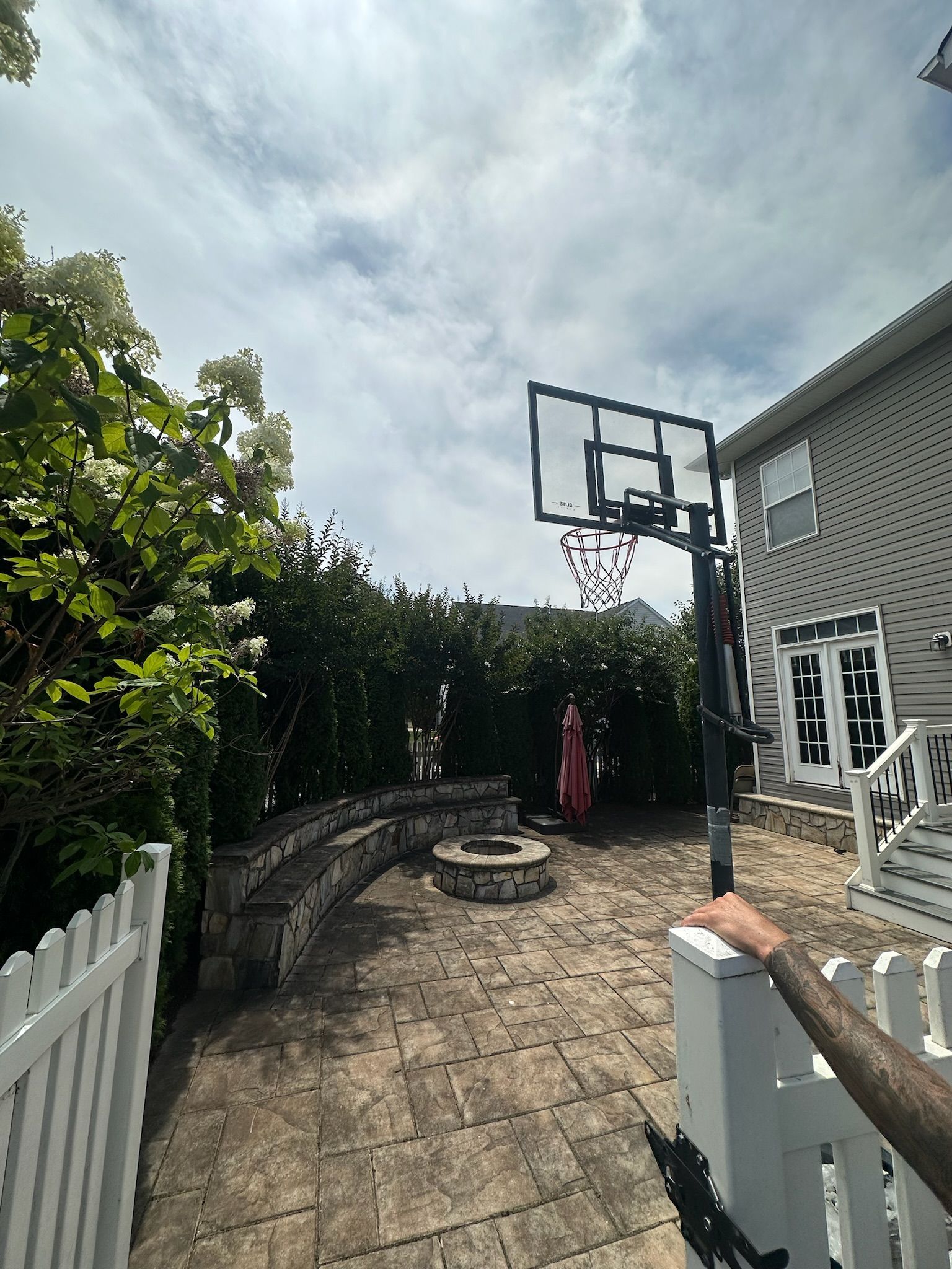 A person is standing in front of a basketball hoop in a backyard.