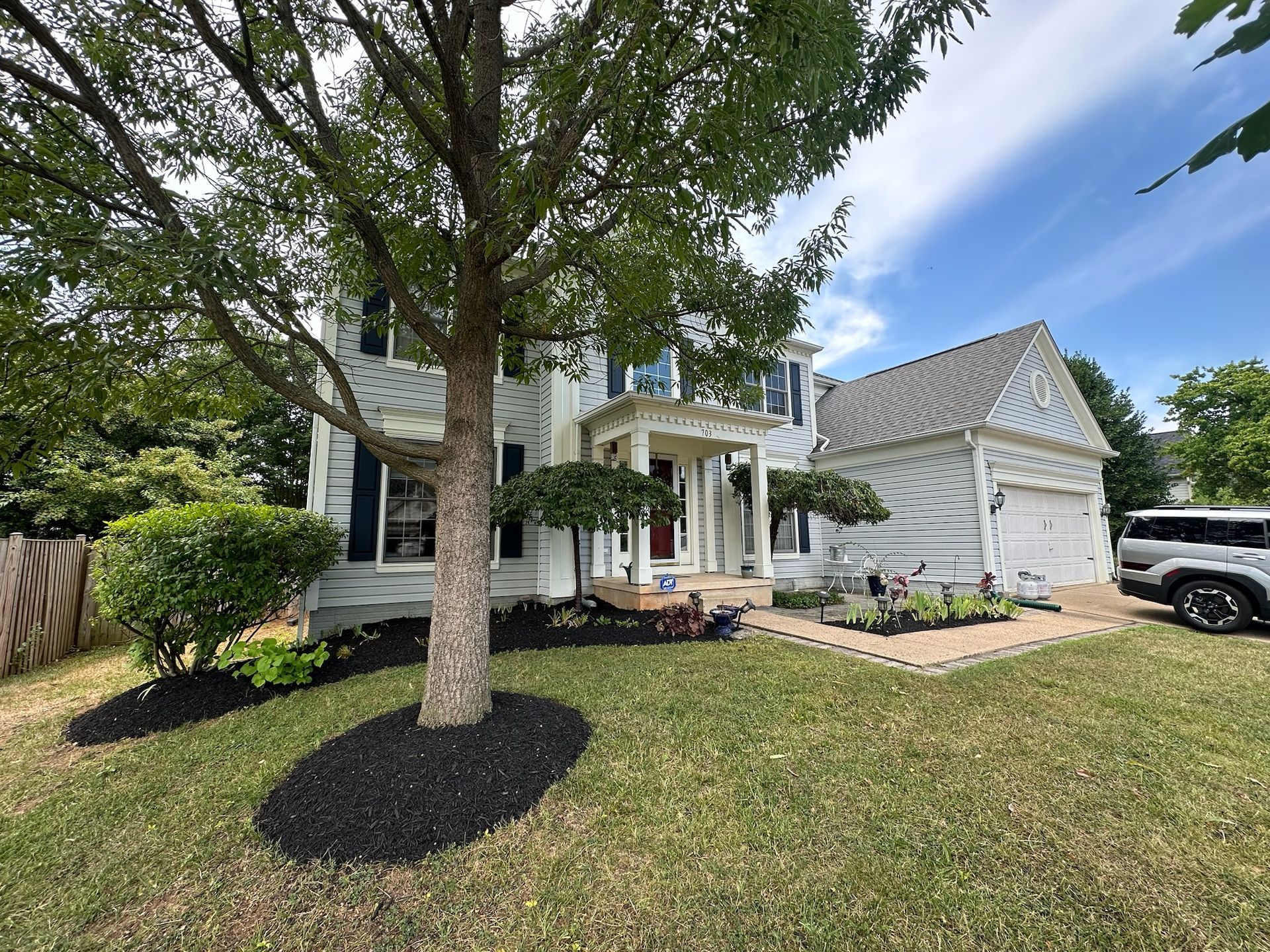 A white house with a tree in front of it and a car parked in front of it.