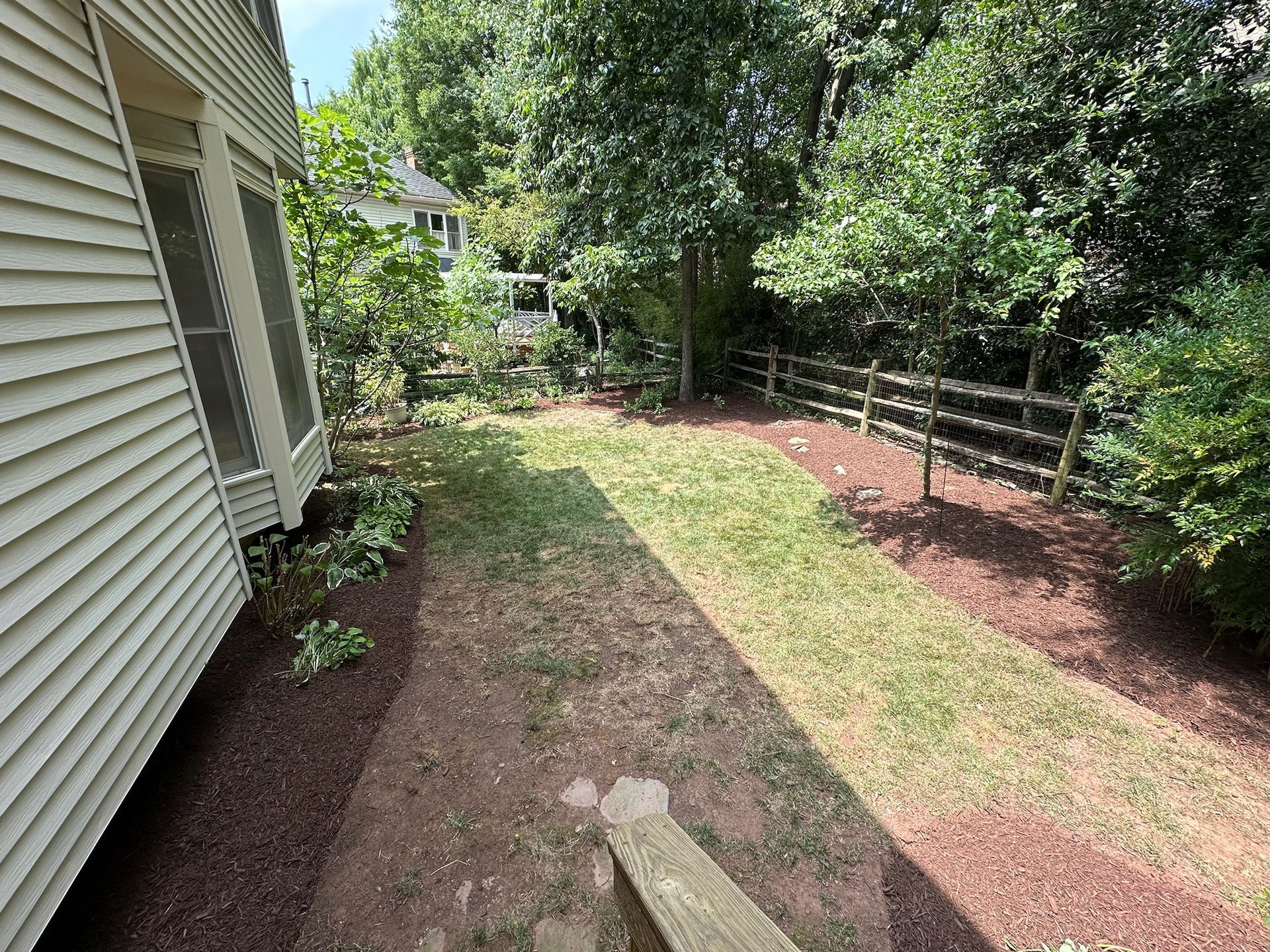 The backyard of a house with a fence and a lush green lawn.