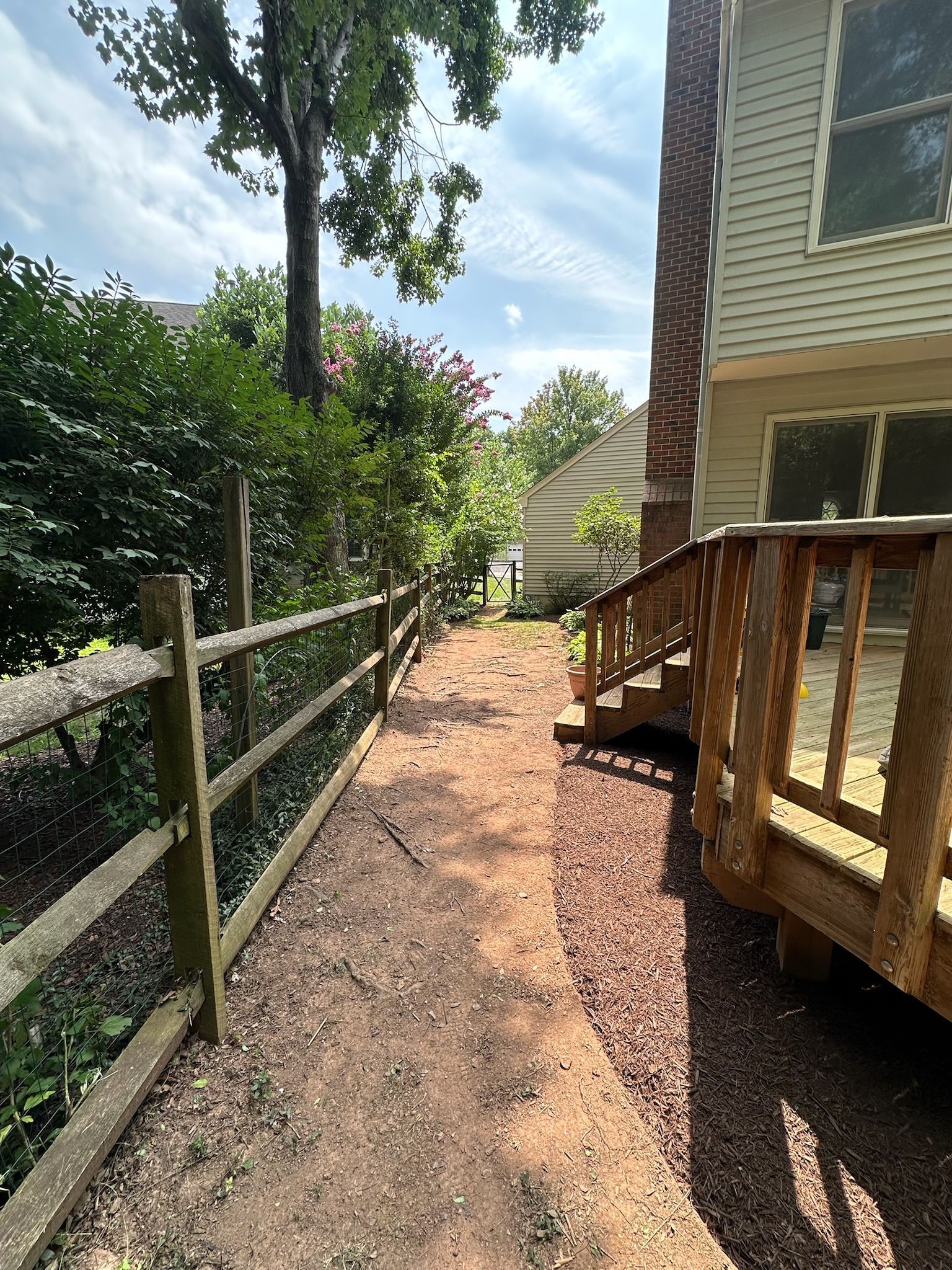 A wooden fence surrounds a dirt path leading to a house.