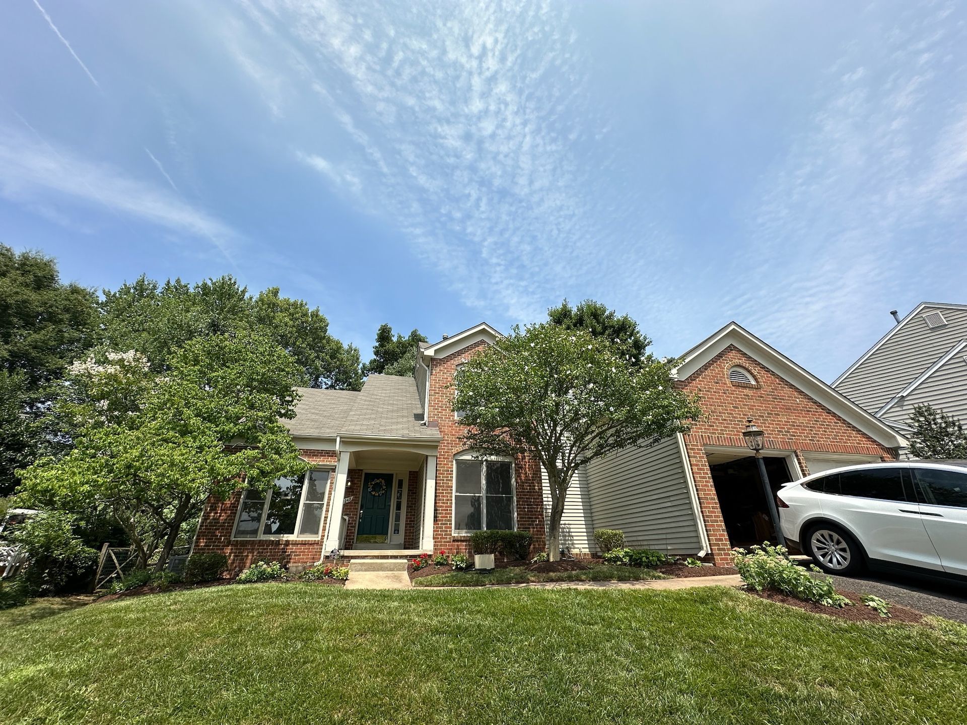A white car is parked in front of a brick house.