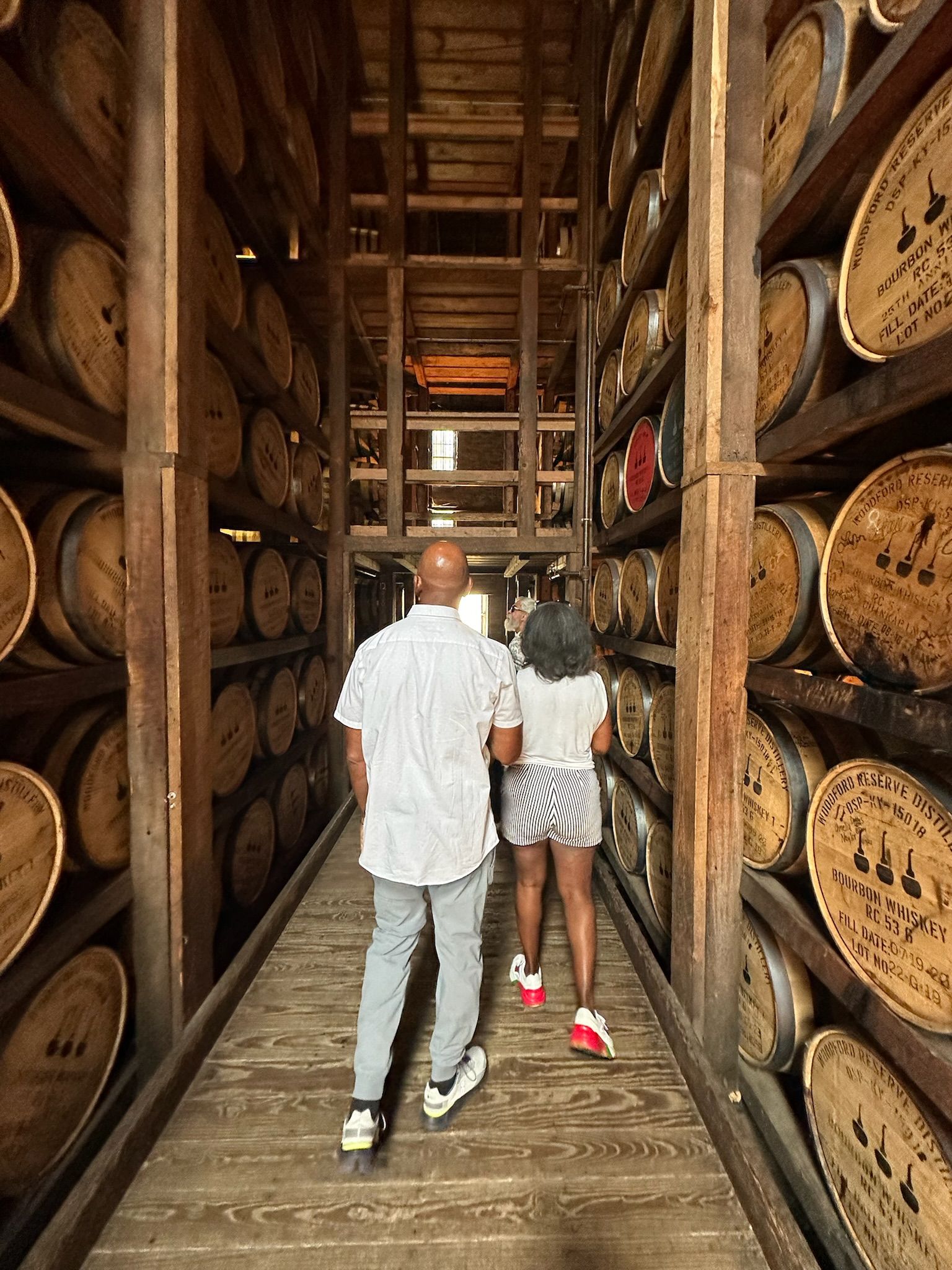 A man and a woman are walking down a wooden hallway filled with barrels.