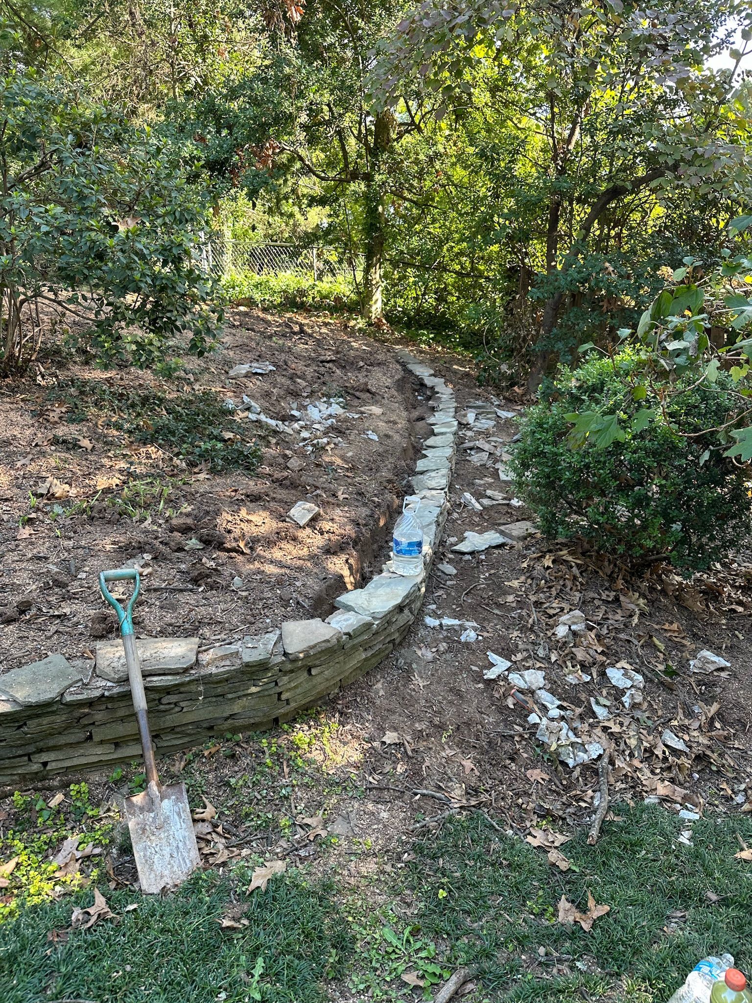 A shovel is sitting on the ground next to a stone wall.