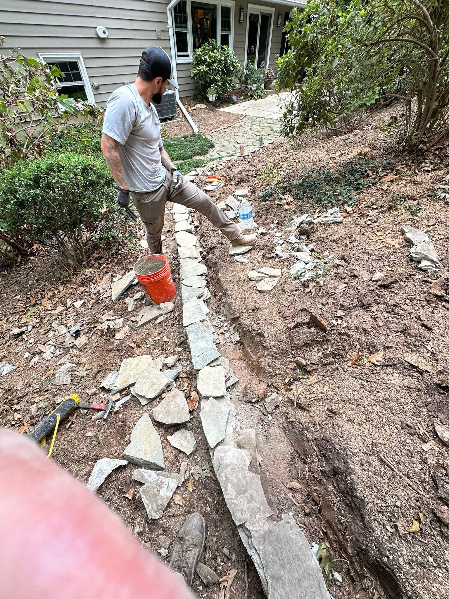 A man is standing next to a stone wall in a yard.