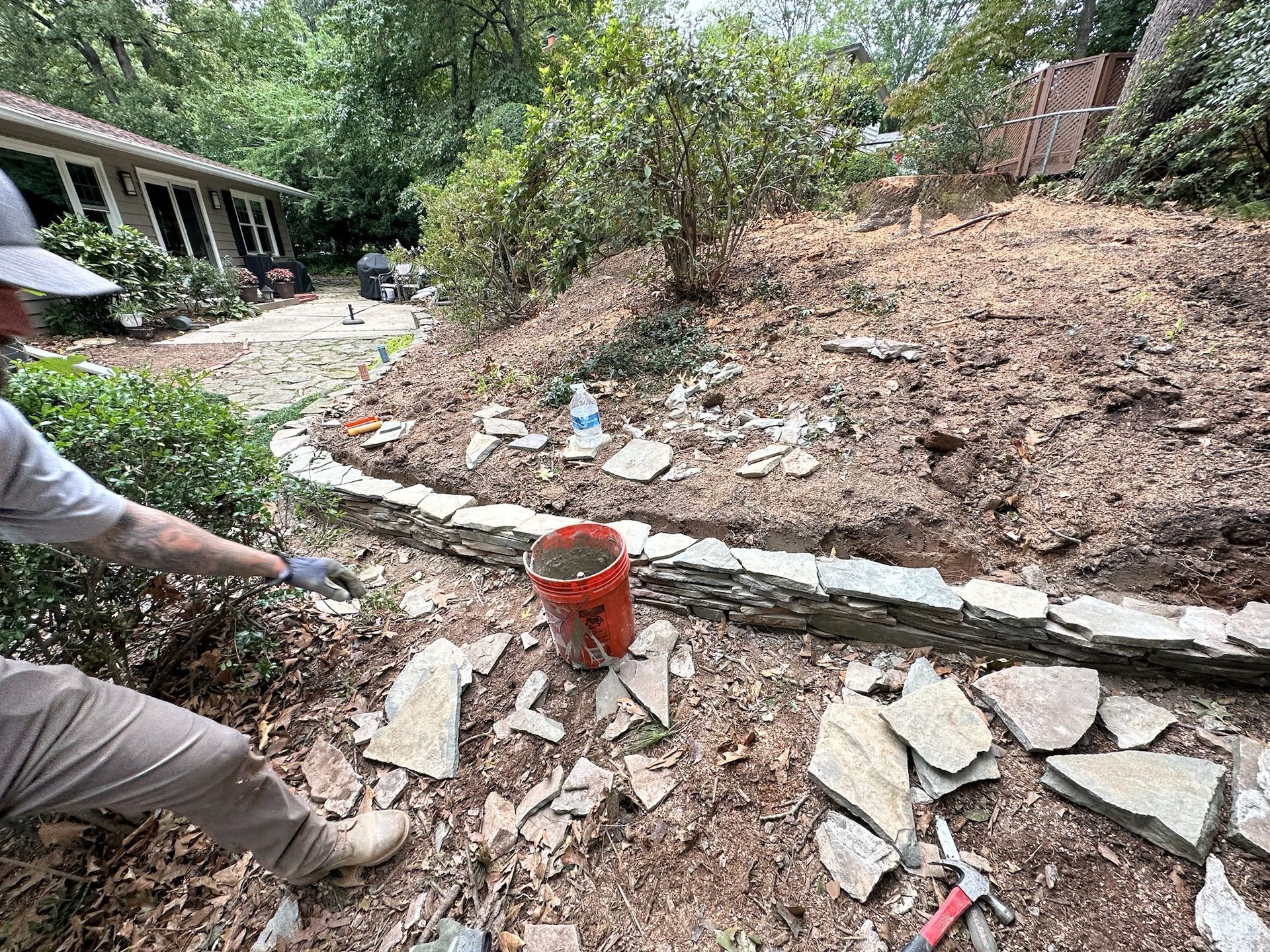 A man is working on a stone wall in a garden.
