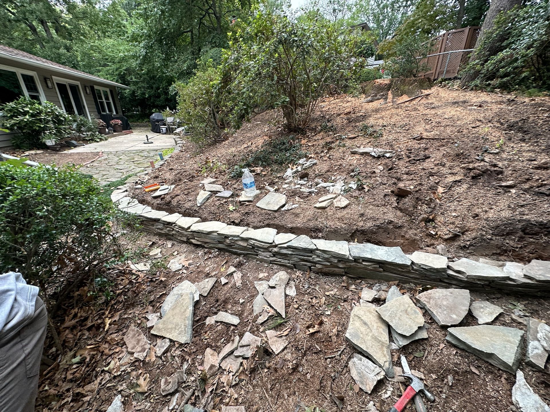 A stone wall is being built in the backyard of a house.