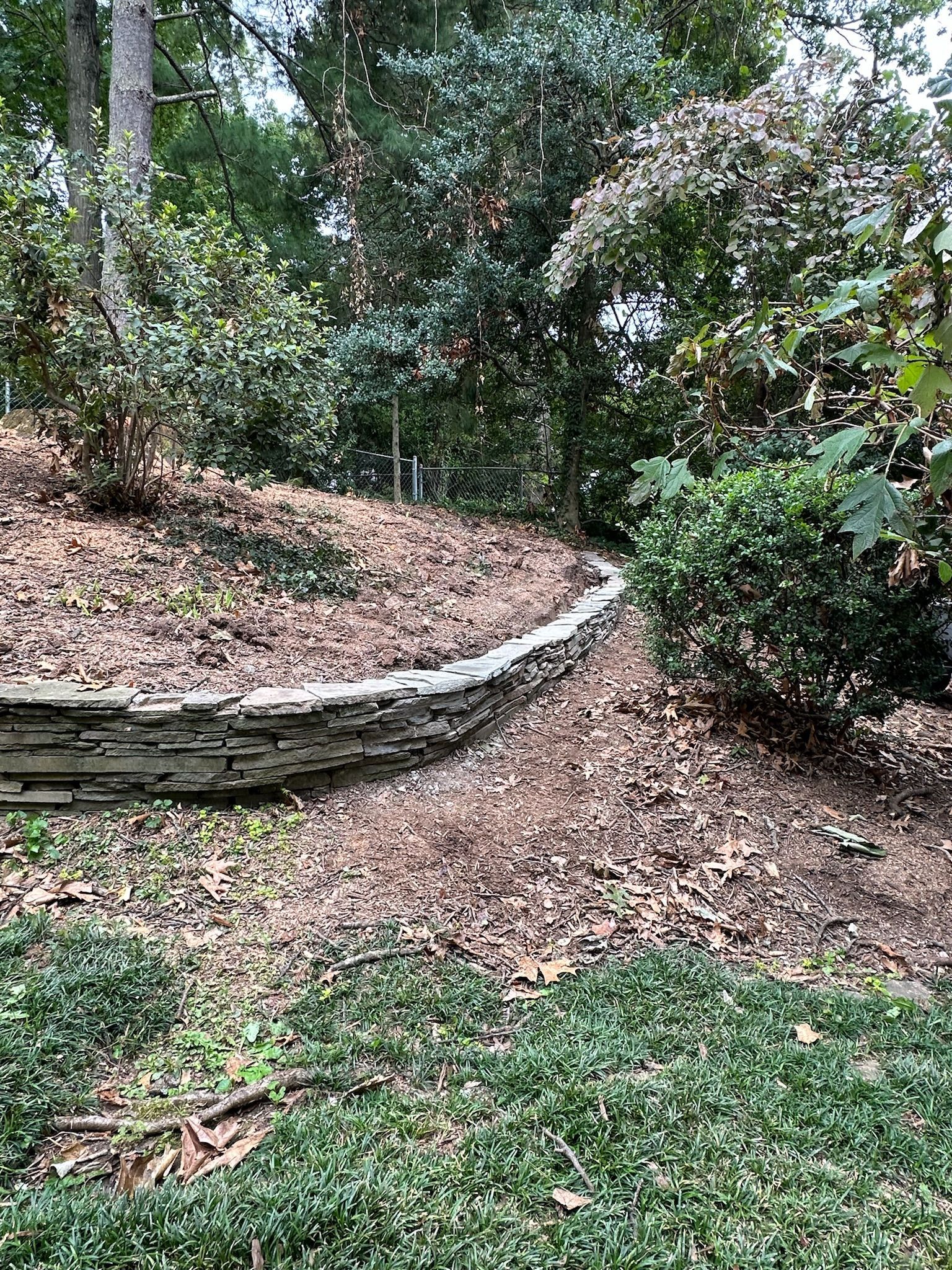 A stone wall is surrounded by trees and leaves in a garden.