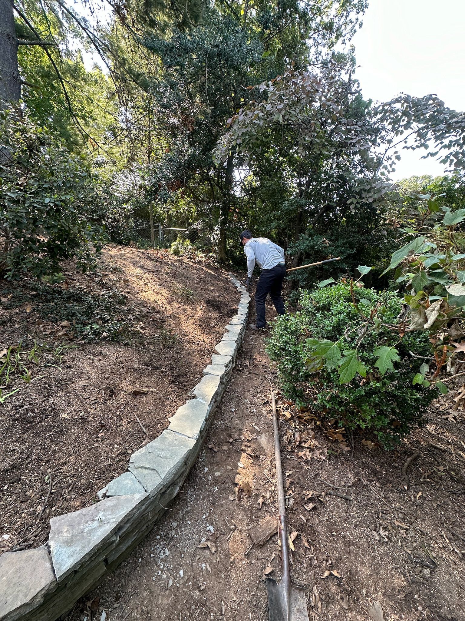 A man is digging in the dirt next to a stone wall.
