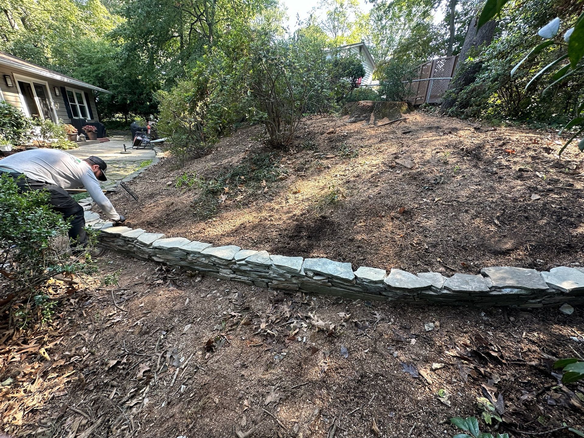 A man is working on a stone wall in a yard.
